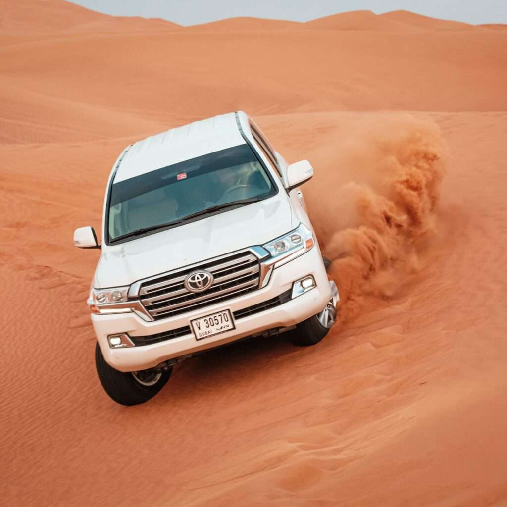 white vehicle driving on the desert sand